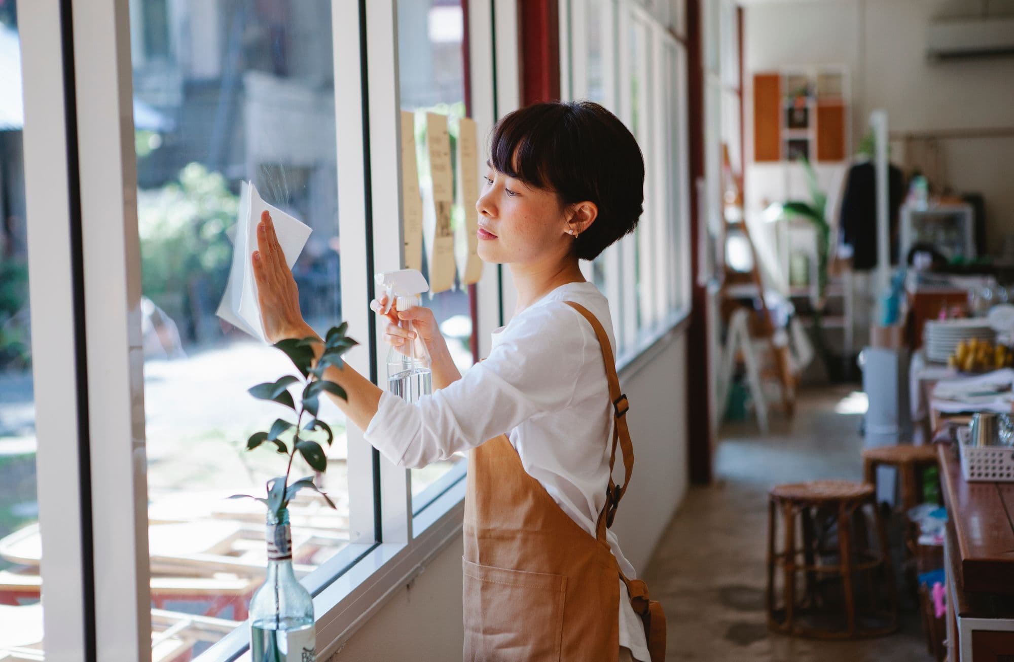 A cafe owner wiping down the front window of her newly opened space in the morning light