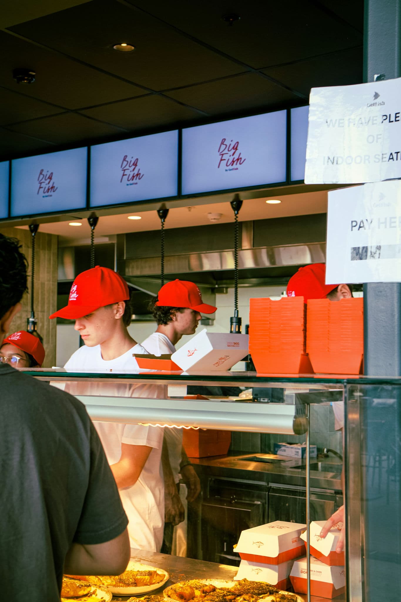 Workers in red hats serving takeaway orders behind a counter at Sydney Fish Market, illustrating the busy direct-order channels Australian restaurants rely on alongside Uber Eats and DoorDash.
